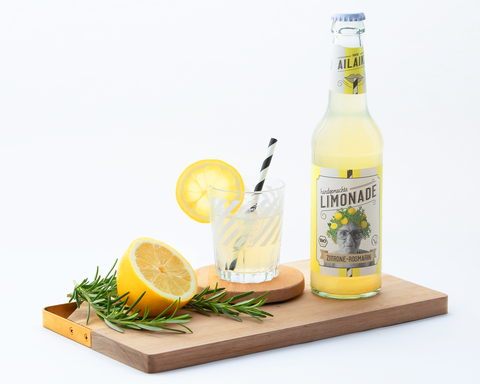 bio-limonade-Zitrone-Rosmarin-steht auf einem Brett neben einem Glas daneben liegen die Zutaten: Zitrone und Rosmarin